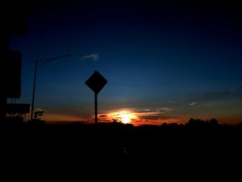 Silhouette road sign against sky during sunset