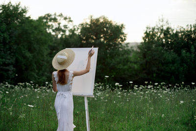 Woman wearing hat standing on field against trees