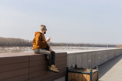Side view of man sitting on railing against clear sky