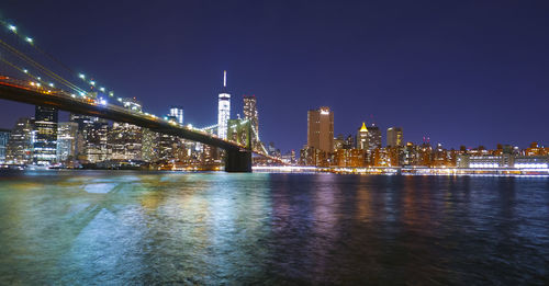 Illuminated city by river against sky at night