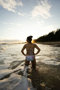 Rear view of shirtless man standing at beach against sky during sunset