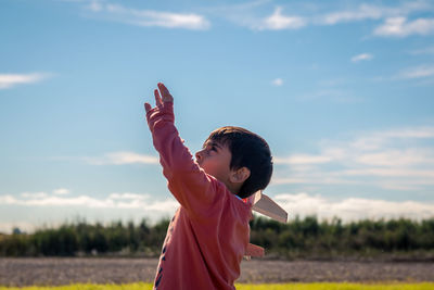 Boy with arms raised against sky