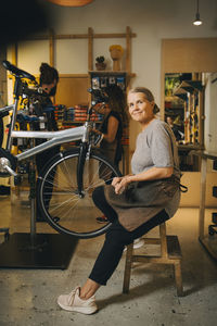 Portrait of smiling female mechanic sitting on table in bicycle shop