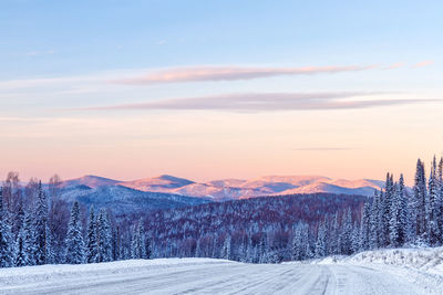 Snow covered landscape against sky during sunset