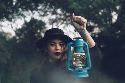 Portrait of woman holding old lantern against trees