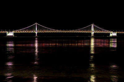 Illuminated bridge over river against sky at night