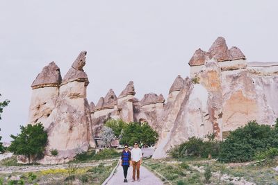 Couple walking on footpath by rock formations against clear sky at cappadocia