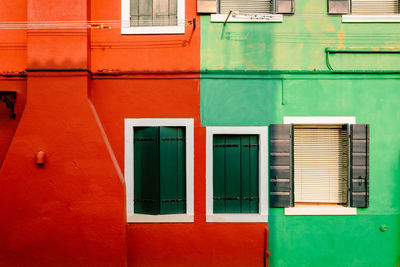 Exterior facade with windows of houses colored red and green in burano