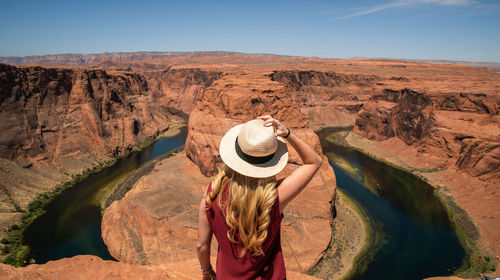 Rear view of woman standing on rock against sky