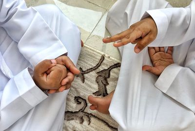 Midsection of friends playing rock paper scissors while sitting on carpet at home