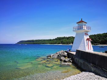 Lighthouse by sea against clear blue sky