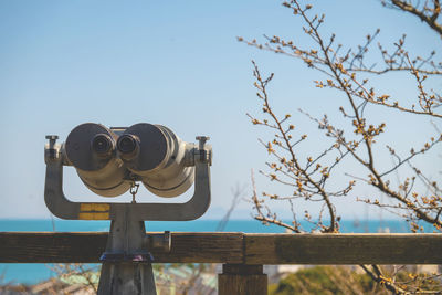 Close-up of coin-operated binoculars by railing against clear sky during sunny day