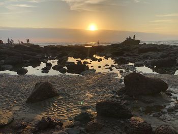 Rocks on beach against sky during sunset