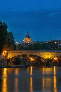 Illuminated bridge over river by buildings against sky at night