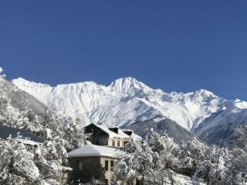 Houses on snowcapped mountain against clear blue sky