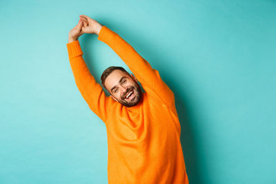 Smiling man with arms raised standing against blue background