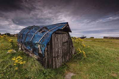 Upturned boat shed on field against moody sky