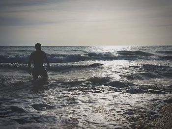 Rear view of silhouette man on beach against sky during sunset