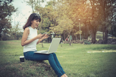 Young woman doing online shopping while sitting on grassy field