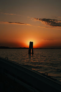 Silhouette standing by sea against sky during sunset