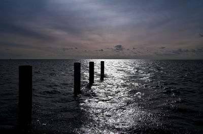 Wooden posts in sea against sky at sunset