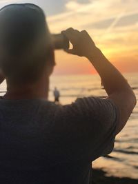 Rear view of man photographing sea at sunset