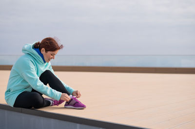 Full length of smiling woman tying shoelace sitting outside