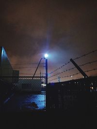 Illuminated street lights and silhouette buildings against sky at night