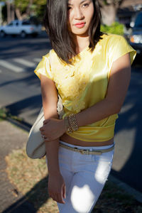 Close-up of smiling young woman holding yellow while standing outdoors
