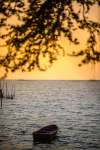 Boat moored in sea against sky during sunset