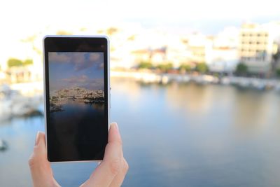 Cropped image of hand photographing city through smart phone