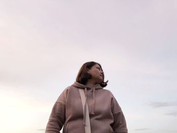 Low angle view of young woman looking away against sky during sunset