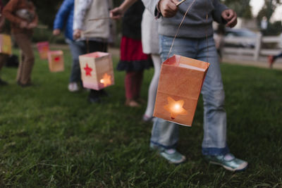 Low section of children carrying illuminated paper lanterns while walking on field