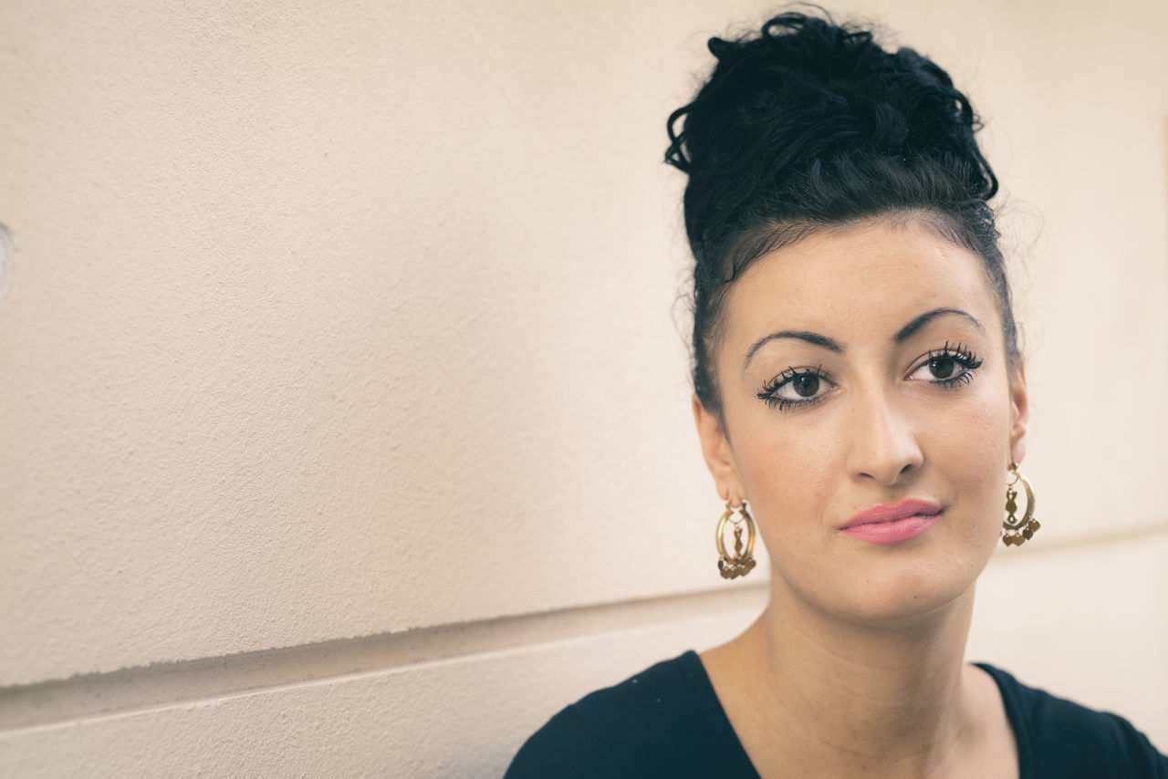 PORTRAIT OF YOUNG WOMAN WITH EYES CLOSED IN FRONT OF WALL