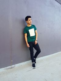 Full length portrait of young woman standing against wall