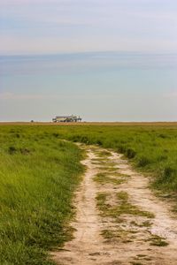 Dirt road amidst field against sky