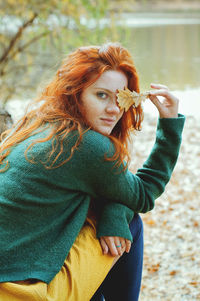 Portrait of redhead woman with freckles  holding leaf outdoors