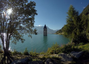 Tower in lake by trees against sky on sunny day