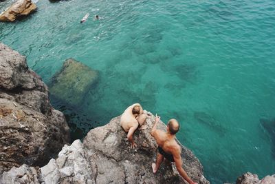 High angle view of shirtless friends on cliff by sea