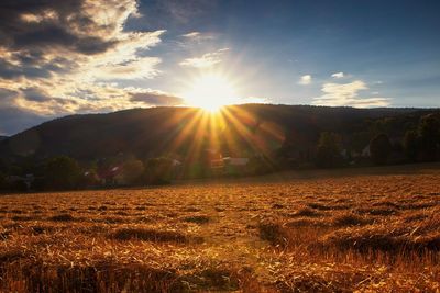 Sunlight streaming on field against sky during sunset