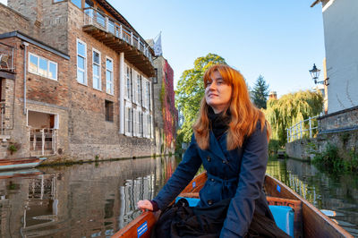 Smiling beautiful woman boating on canal amidst buildings