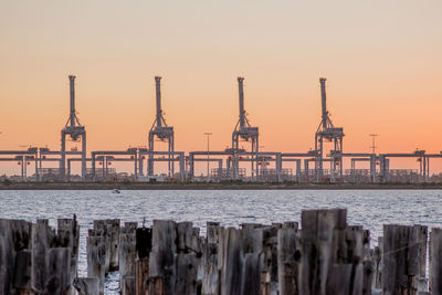 Cranes at harbor against clear sky during sunset