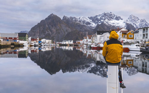 Norway, northern norway, henningsvaer, back of hooded man sitting on top of pole at coast of fishing village in lofoten archipelago