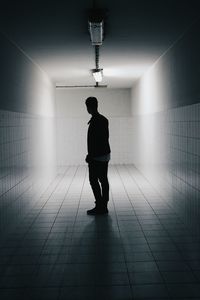 Rear view of silhouette man standing on illuminated walkway