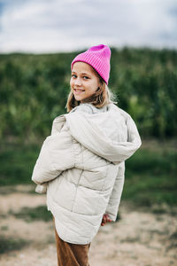 Cheerful beautiful teenage girl in a yellow raincoat and a pink hat is dancing on the background 