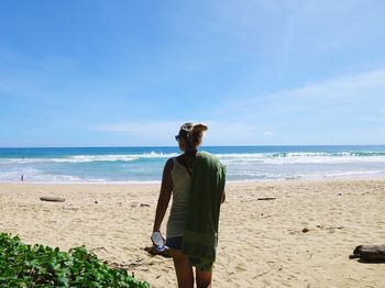 Rear view of woman standing at naithon beach against blue sky