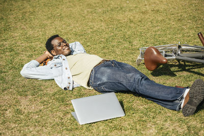 Young man with bicycle, relaxing, lying on grass