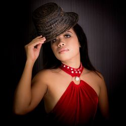 Portrait of beautiful young woman wearing hat against black background