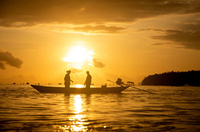 Silhouette fishermen on wooden boat preparing casting a net catching fish in the early morning