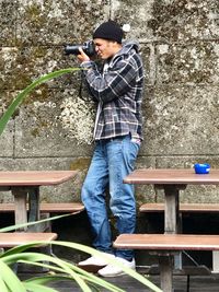 Side view of young man holding camera while standing outdoors